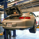 A silver 2003 Porsche 911 on a car hoist is being inspected.